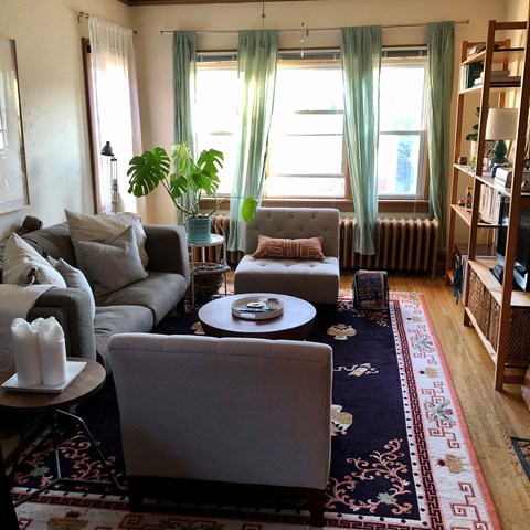 A living room with a grey couch, a round table, and a large window with curtains.