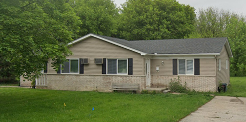 a tan brick house with black shutters and a bench