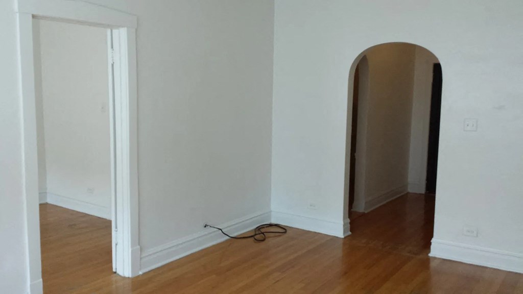 an arched doorway in an empty room with wooden flooring and a cable plugged