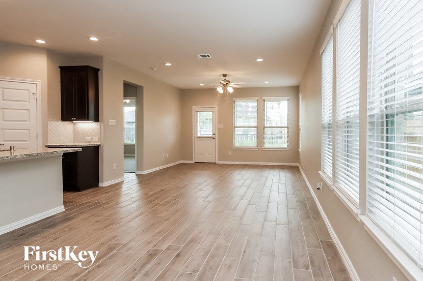 an empty living room with a kitchen and large windows