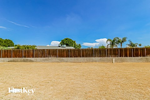 A wooden fence in the foreground with a blue sky and some trees in the background.