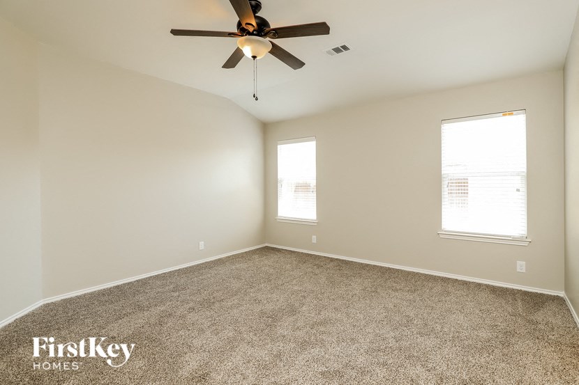 an empty room with a ceiling fan and two windows