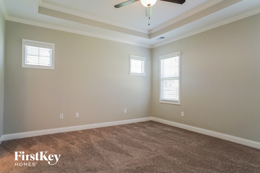 a carpeted living room with a ceiling fan and two windows