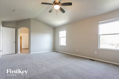 A spacious room with a ceiling fan and two windows.