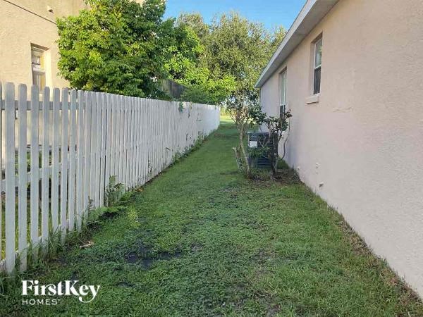 A white picket fence separates a grassy area from a house.