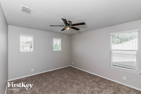 A room with a carpet floor, a ceiling fan, and two windows.