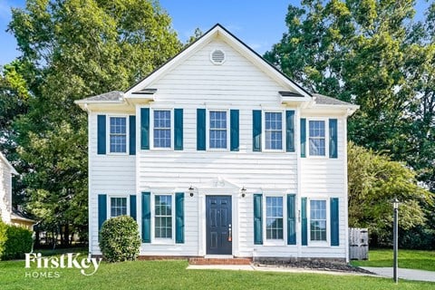 A white house with a black door and green shutters.
