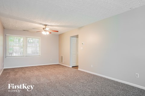 A room with a carpet floor, a ceiling fan, and a door.