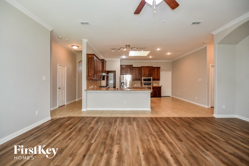 an empty living room with a kitchen and a ceiling fan