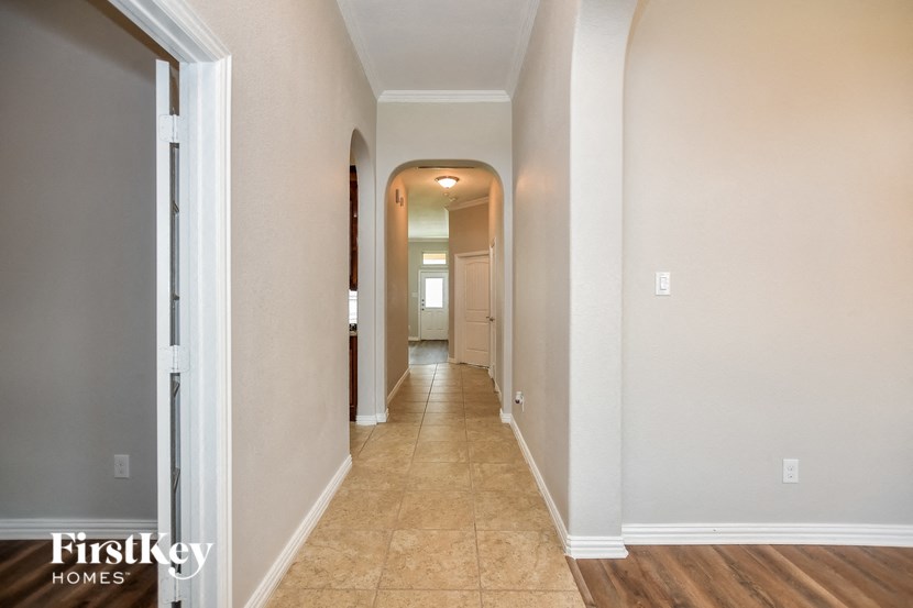 a hallway with white walls and a tiled floor and a door to a house
