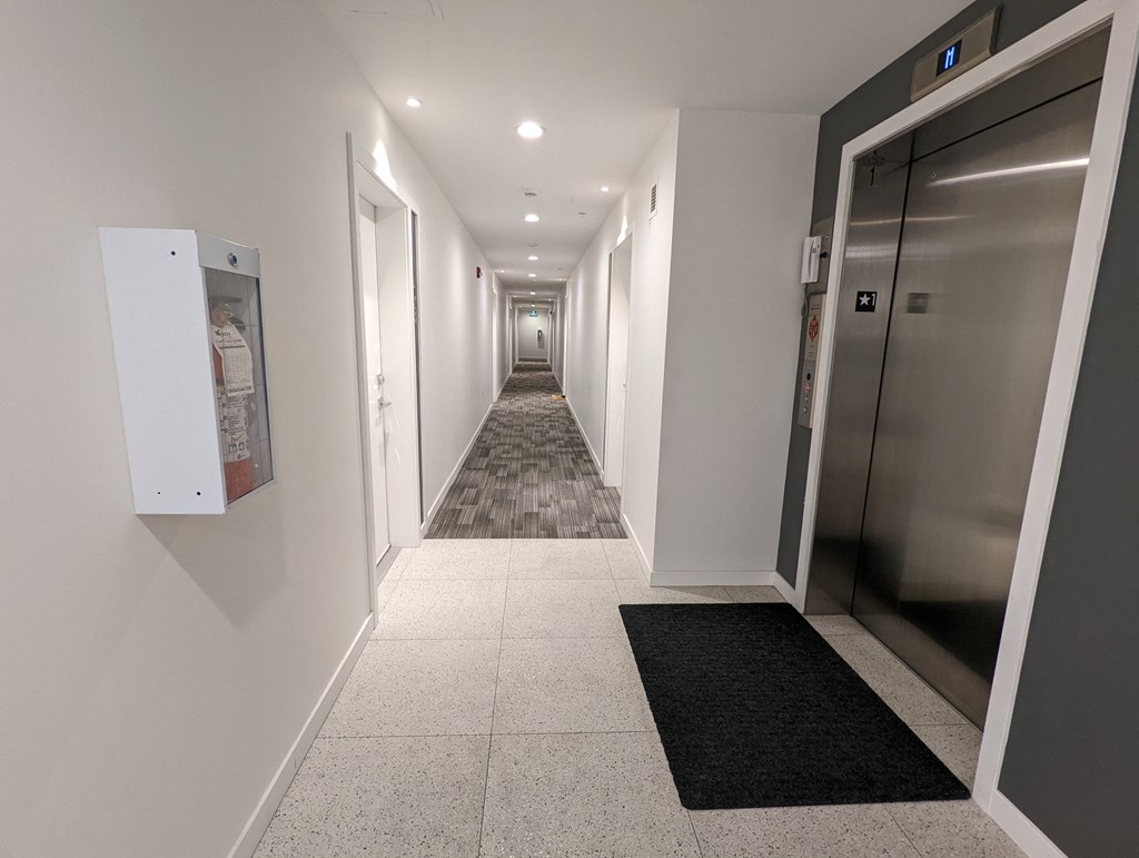 A long hallway with a black mat in front of a silver elevator.