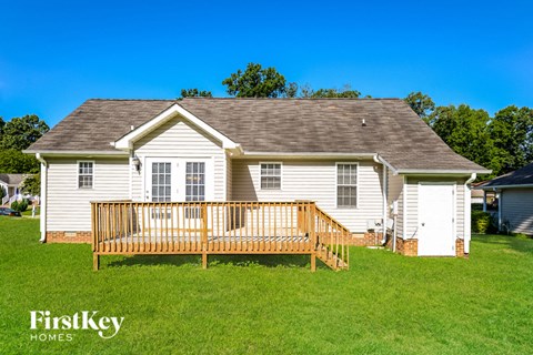 A house with a white exterior and a brown roof with a deck in front.