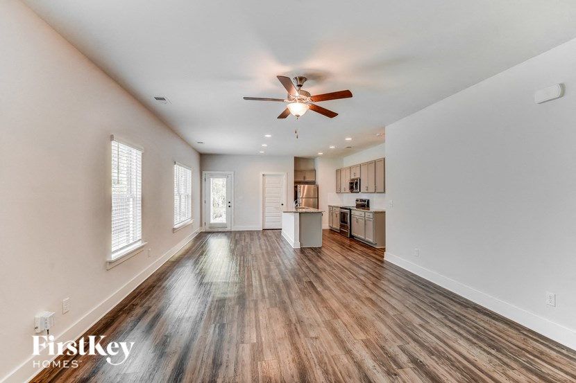 an empty living room with a ceiling fan and a kitchen