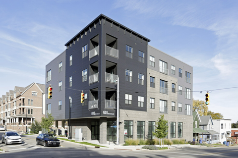 A modern multi-story building with a black facade is situated on a street corner with cars and traffic lights visible.