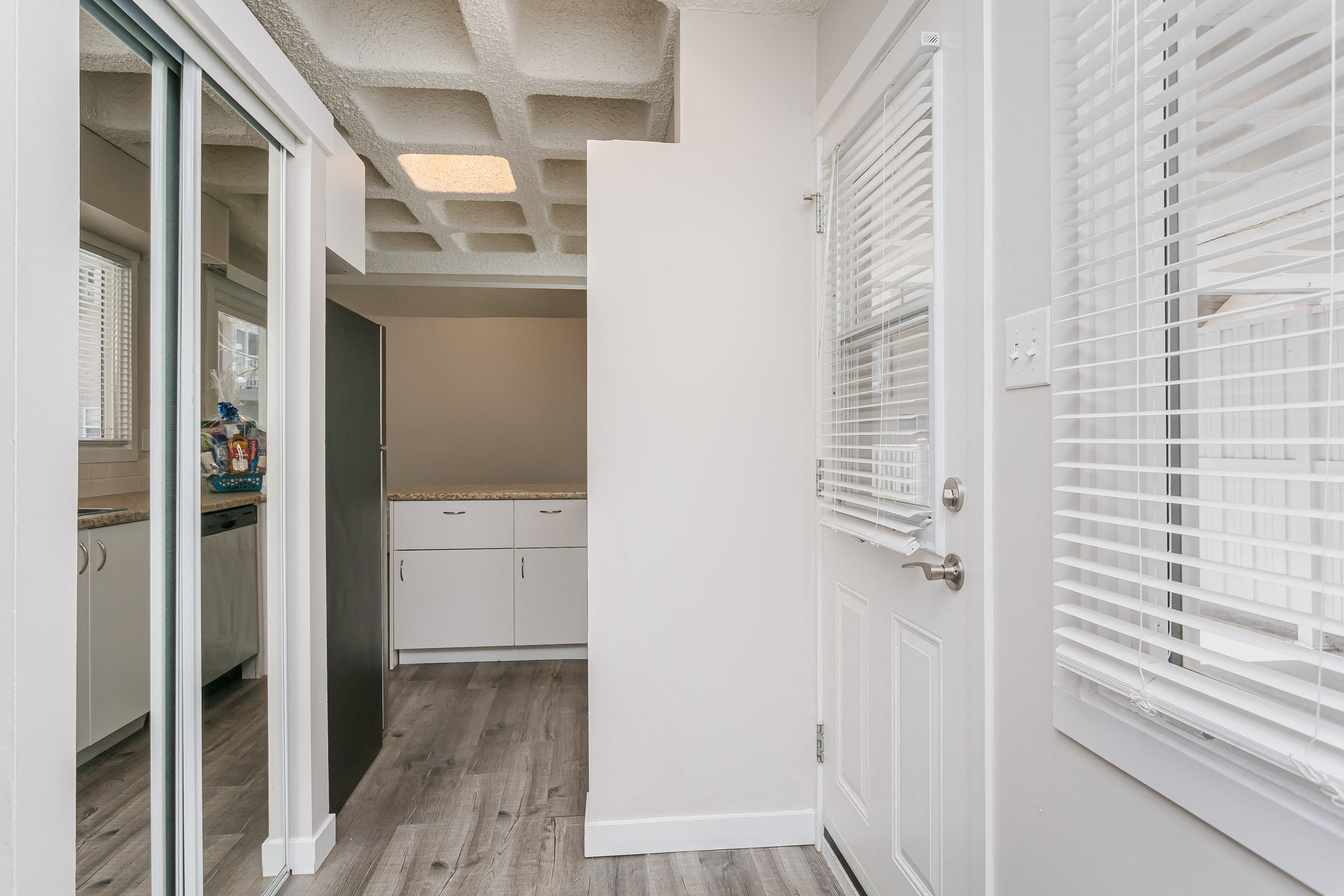 a renovated living room with white blinds and a door to a kitchen