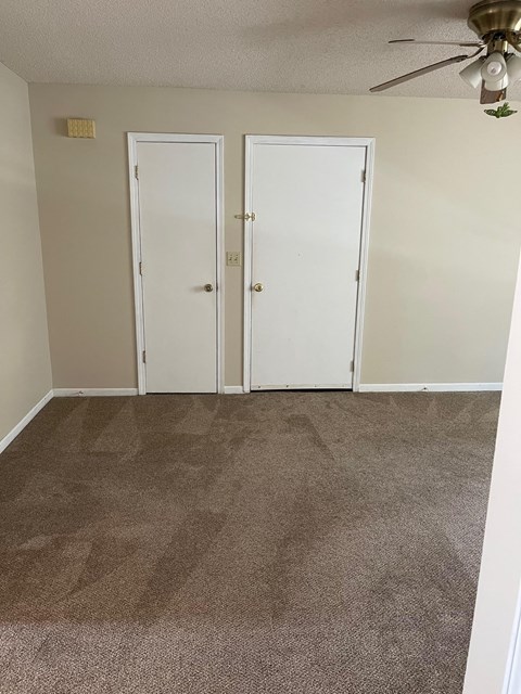 a carpeted room with two doors and a ceiling fan