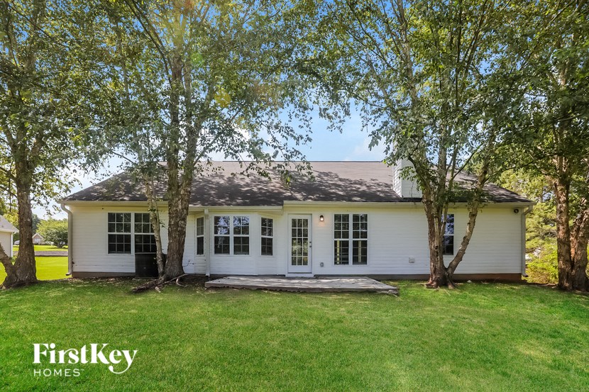 A white house with a black door and windows is surrounded by trees.