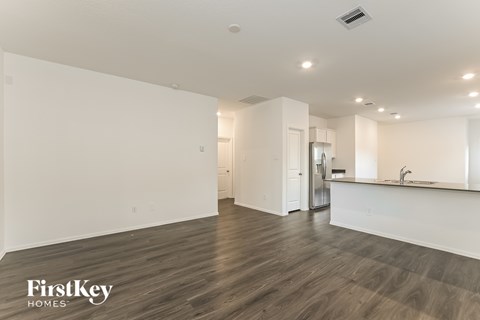 A spacious room with wooden flooring and a kitchen area with white cabinets and a countertop.