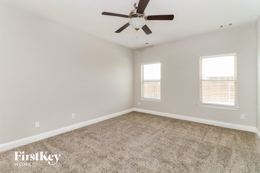 A spacious room with a ceiling fan and two windows.