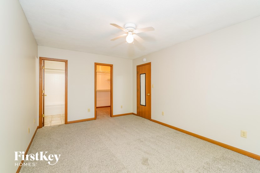 A carpeted room with a ceiling fan and two doors.