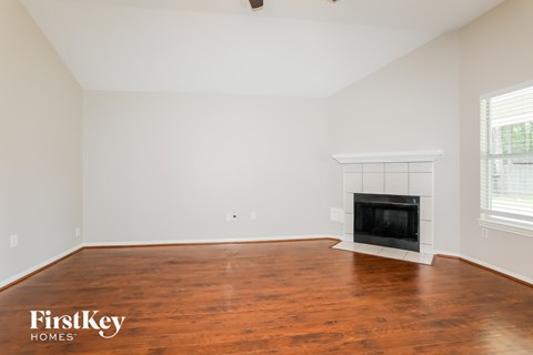 A large empty room with a fireplace and wooden floors.
