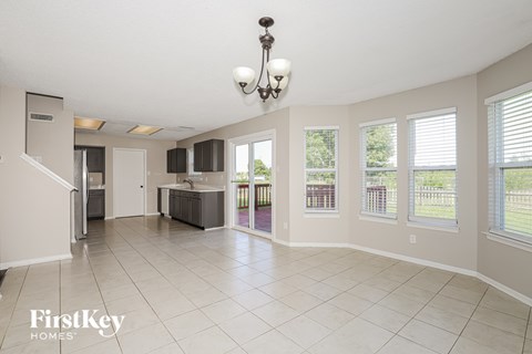 A spacious living room with a kitchen in the background and a chandelier hanging from the ceiling.