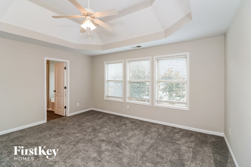an empty living room with a ceiling fan and three windows