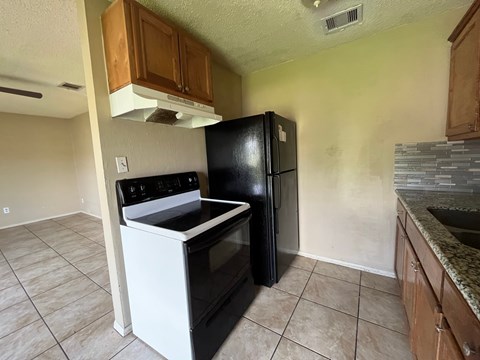 A black refrigerator stands in a kitchen next to a stove.