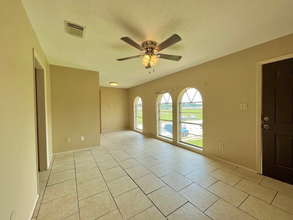 an empty living room with a ceiling fan and tiled floors