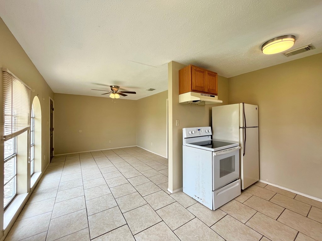 an empty kitchen with a stove refrigerator and a ceiling fan