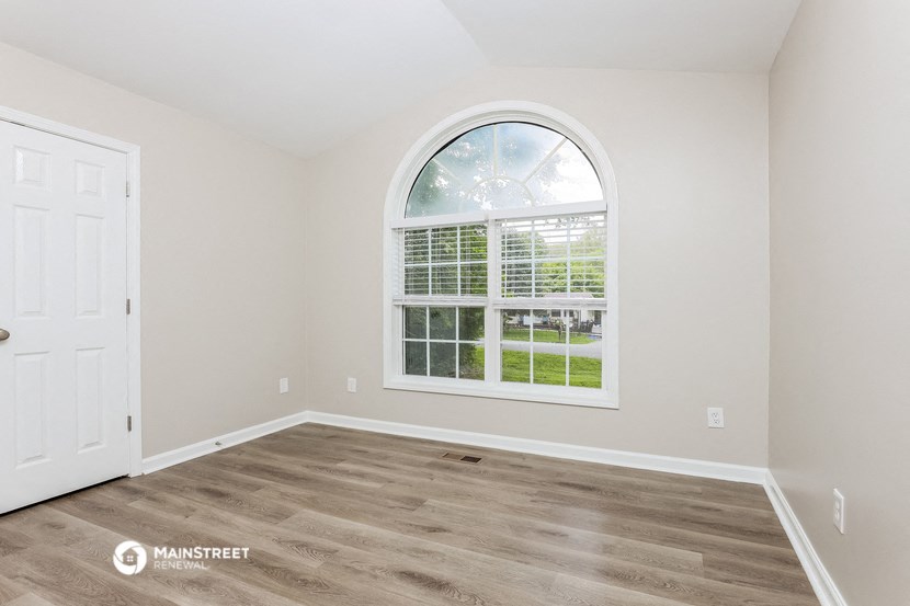 an empty bedroom with a large window and wood flooring