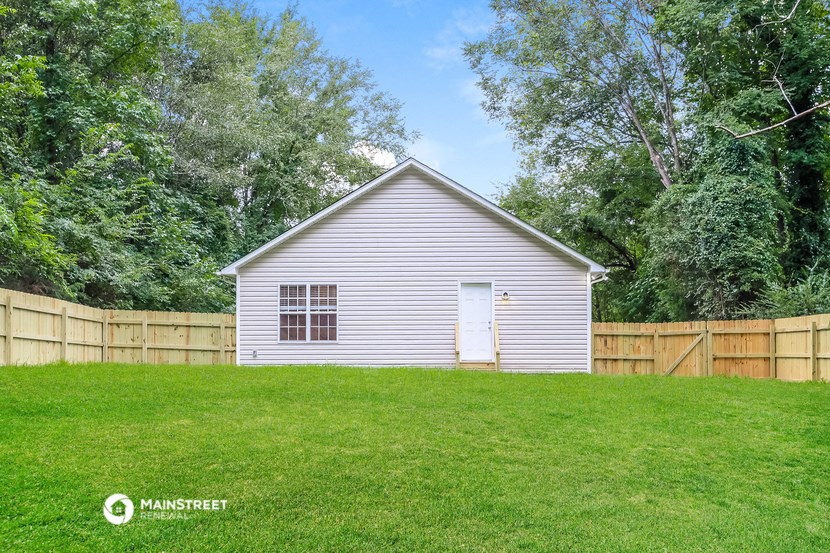 a small white house with a wooden fence and a grass field
