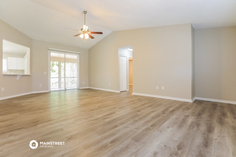 the spacious living room with hardwood flooring and a ceiling fan