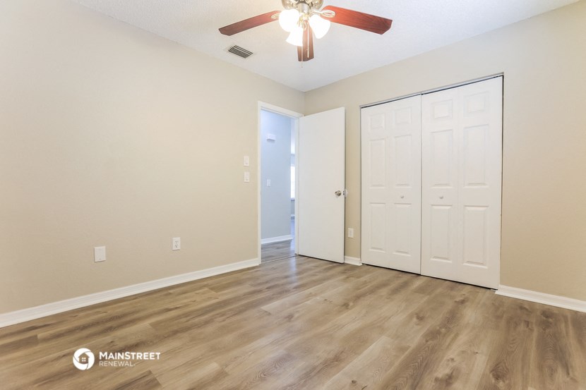 the spacious living room with a ceiling fan and a door to the bedroom