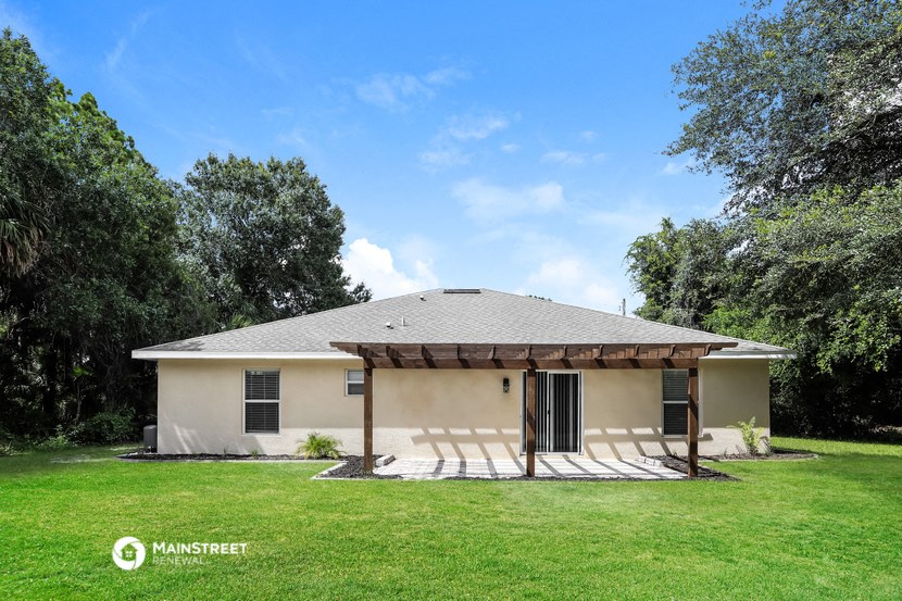 a small tan house with a covered porch and a grassy yard
