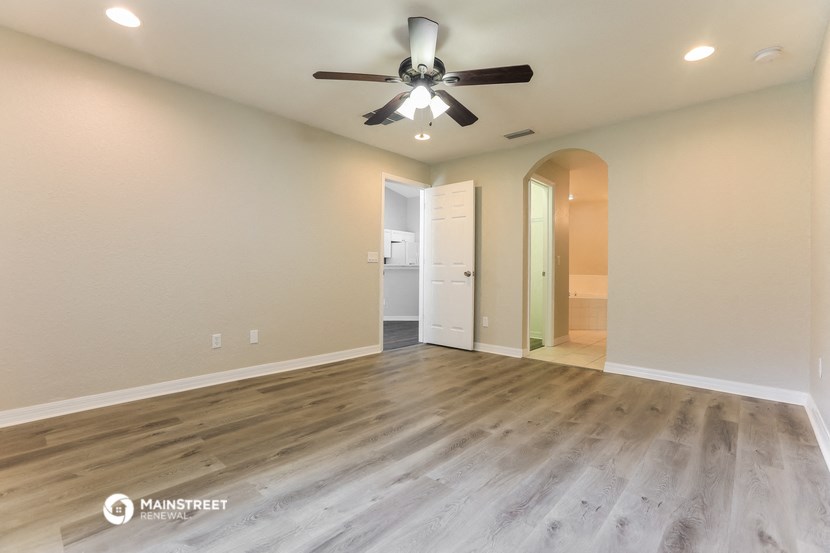 the spacious living room with hardwood flooring and a ceiling fan