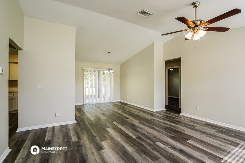 the spacious living room with wood flooring and a ceiling fan