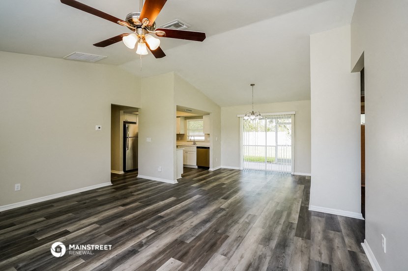 the living room and kitchen of an empty house with a ceiling fan