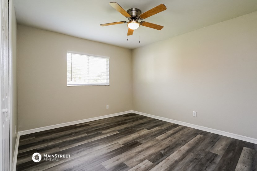 the spacious living room with wood flooring and a ceiling fan