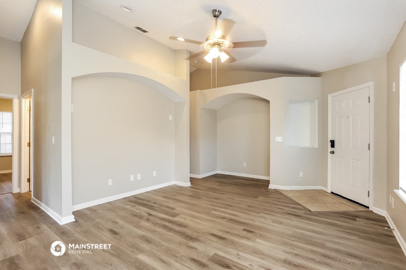 an empty living room with a ceiling fan and a door
