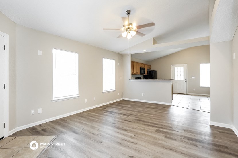 an empty living room with a ceiling fan and a kitchen
