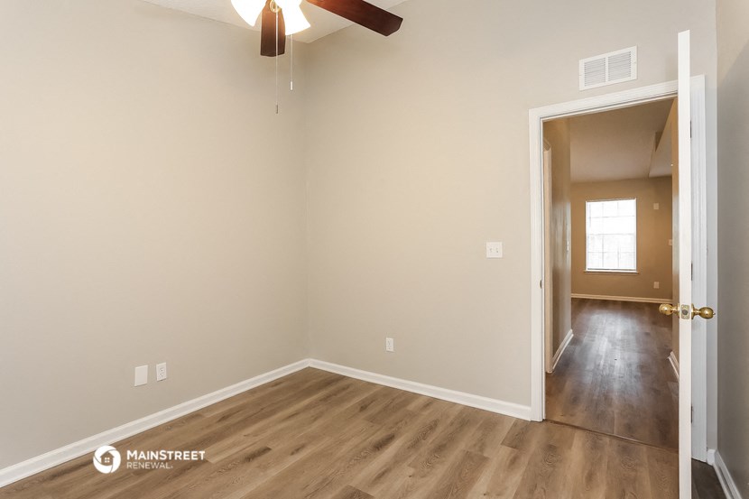 the spacious living room with hardwood flooring and a ceiling fan