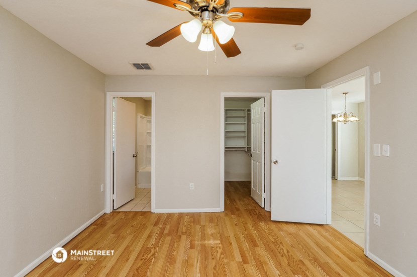 a bedroom with a ceiling fan and a hallway to two closets