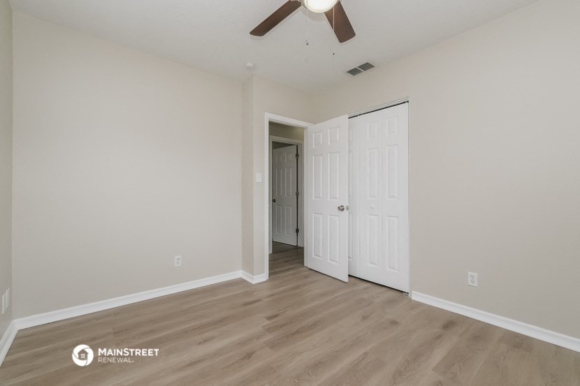the living room of an apartment with white walls and a ceiling fan