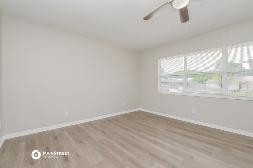 the spacious living room with wood flooring and a ceiling fan