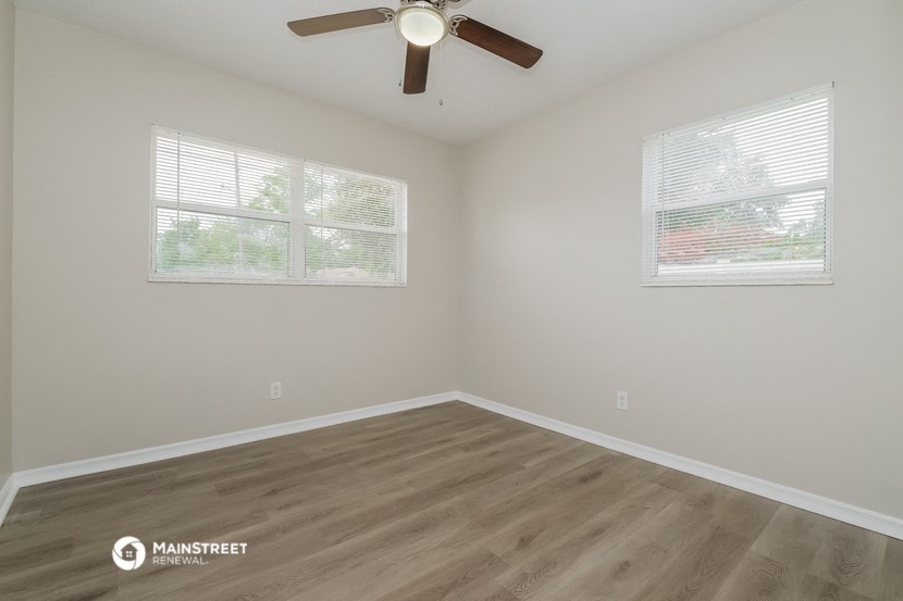 the spacious living room with two windows and a ceiling fan