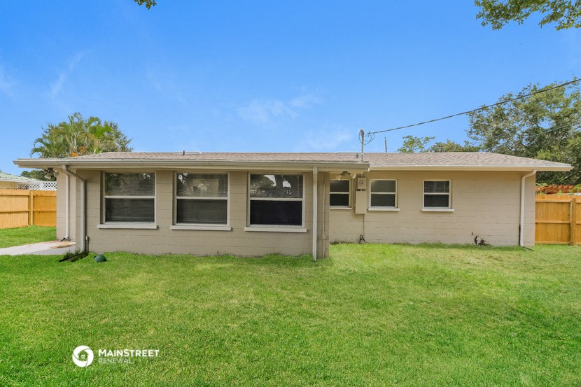 a small tan house with a grassy yard and a wooden fence