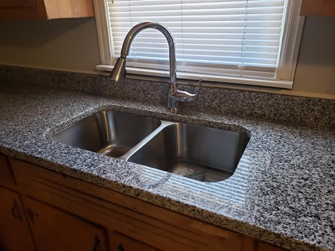 a kitchen sink with granite counter top and a window