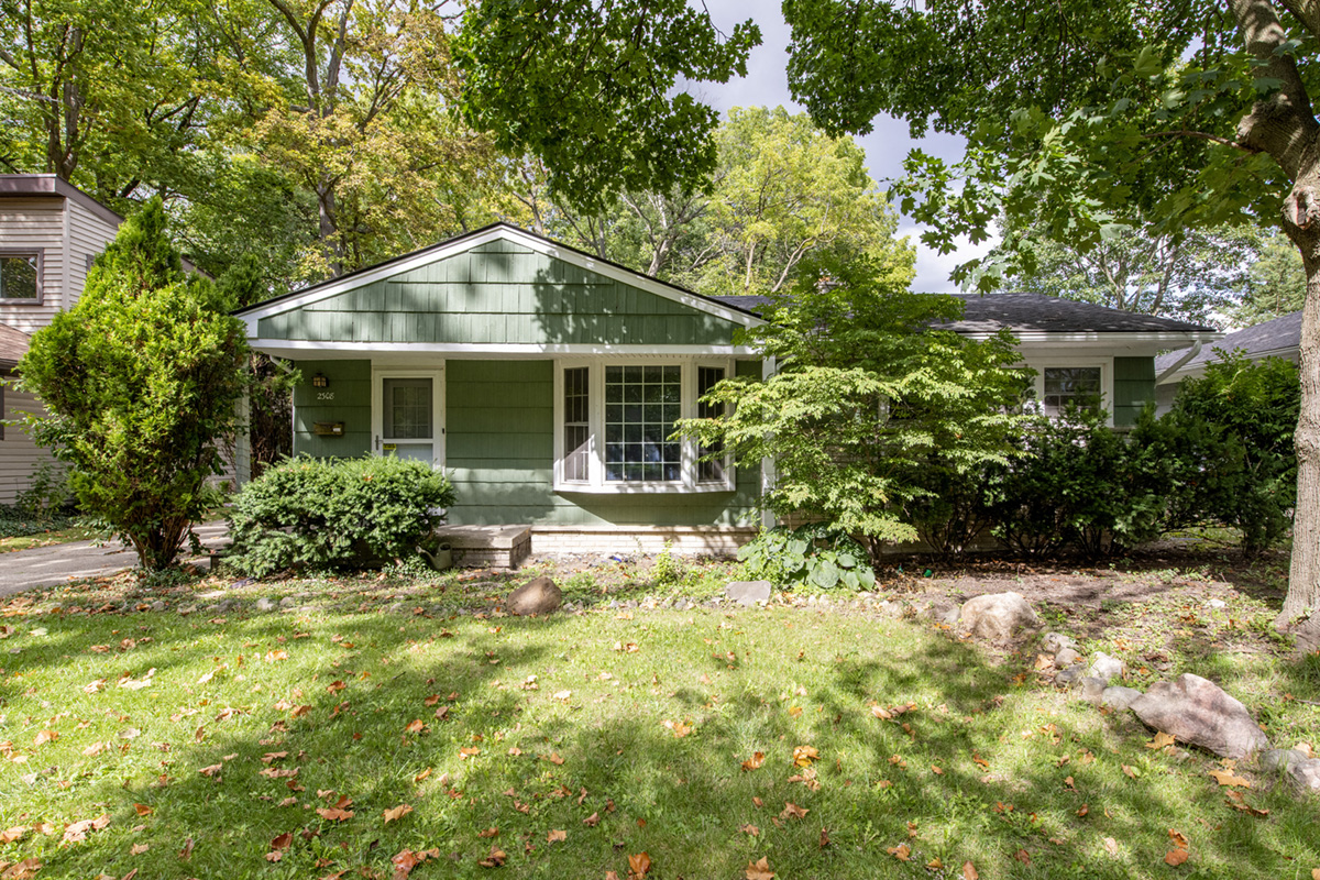 A green house with a porch surrounded by trees and grass.