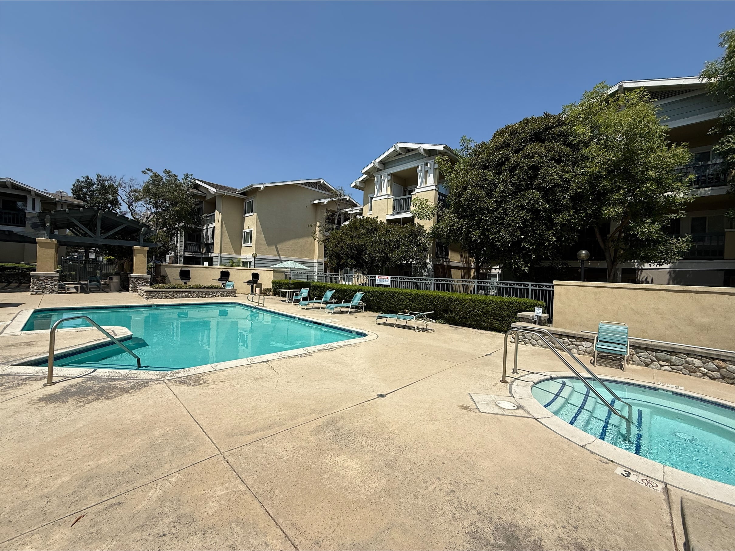 A swimming pool surrounded by a concrete patio and apartment buildings.